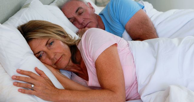 Upset Senior Woman Lying in Bed Next to Sleeping Husband - Download Free Stock Images Pikwizard.com