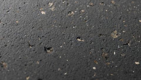 Close-up asphalt surface revealing embedded aggregate and mica flecks, gritty macro texture