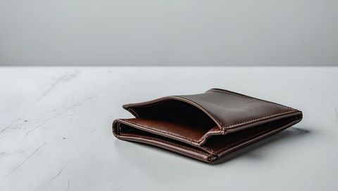 Brown leather bifold wallet on minimal white surface reflecting financial struggles