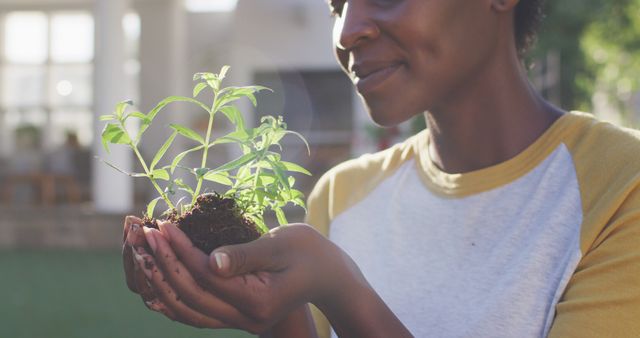 Happy african american female gardening, holding and smelling plant in garden - Download Free Stock Photos Pikwizard.com