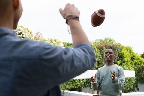 African american friends tossing football on backyard terrace, casual pass and laughter