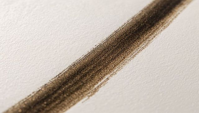 Diagonal bronze brush stroke on textured paper showing granular pigment and surface tooth
