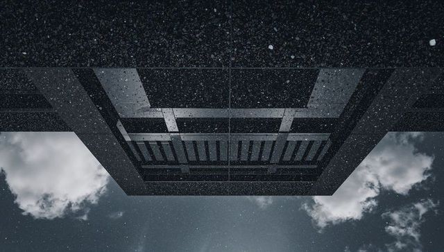 Inverted concrete overhang framing geometric beams recessed panels against cloudy sky