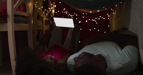 Father and Daughter Watching Tablet in Cozy Fort with Fairy Lights