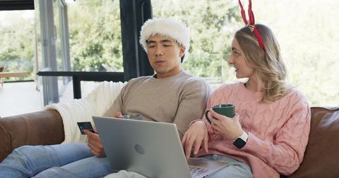 Couple doing online holiday shopping with laptop and credit card wearing santa hat and antlers