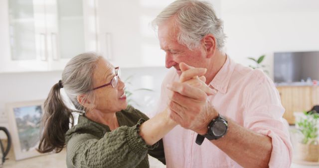 Senior couple dancing closely in a modern kitchen, showing romantic and loving moments. Suitable for use in content focusing on love in later years, senior lifestyle, healthy aging, family happiness, or advertisements for elder care and services.