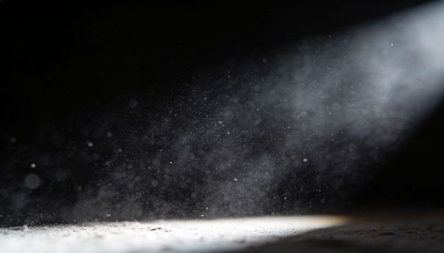 Casting diagonal light shaft revealing dust motes over textured floor in dark interior