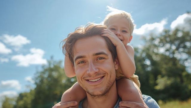 Smiling father carrying toddler on shoulders in sunlit park, candid outdoor family portrait