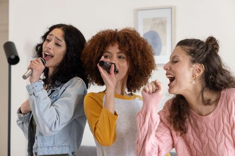 Diverse friends singing karaoke at home holding microphones celebrating music bonds