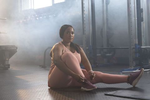 African american woman tying sneaker in gym wearing pink activewear showing determination