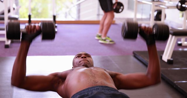 Man lying on gym floor bench pressing dumbbells for chest workout. Developing upper body strength and muscle. Ideal for fitness and health publications, workout blogs, and exercise routine illustrations.