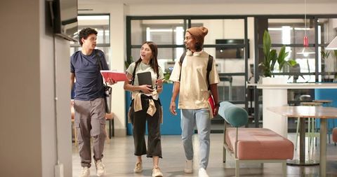 College students walking through campus common area carrying notebooks backpacks and chatting