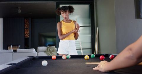 African woman reacting while playing billiards at home on black-felt pool table