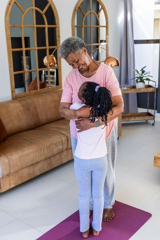 African american grandmother hugging granddaughter on yoga mat at home, cozy family hug