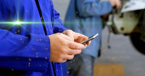 Workshop technician typing on smartphone while wearing blue work jacket near machinery