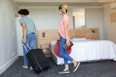 Interracial couple checking into hotel pulling suitcase carrying passport and sun hat
