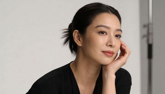 Serene asian woman resting cheek and gazing with poise in studio headshot for branding
