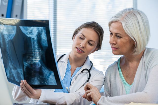 Female doctor showing and explaining an x-ray report to a senior patient in a medical office. Ideal for use in healthcare, medical consultation, patient care, and doctor-patient interaction contexts. Can be used in articles, websites, and brochures related to medical diagnosis, radiology, and health checkups.