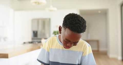 Laughing boy looking down in bright modern kitchen with wooden island and pendant lights