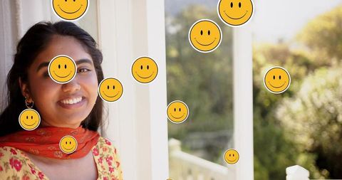 Smiling indian woman in yellow kurta and orange dupatta on sunlit porch with smiley stickers