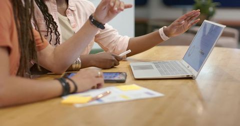 African american colleagues collaborating with laptop and smartphone on wooden table