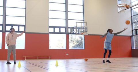 Coach guiding trainee in basketball drill at indoor gym