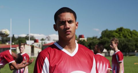 Young rugby player standing on field with team in background