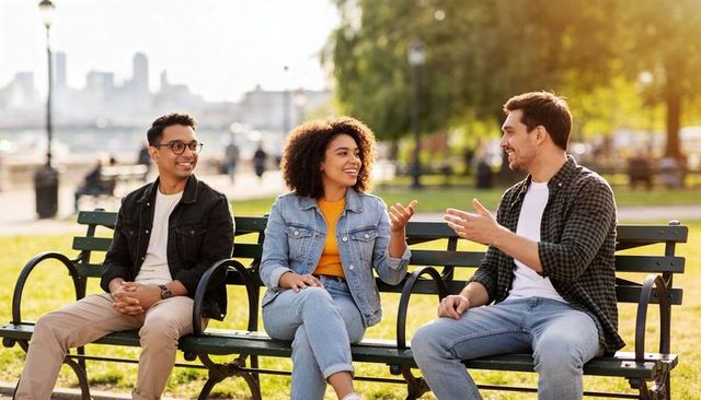 Friends chatting on waterfront bench enjoying sunny urban park conversation and laughter