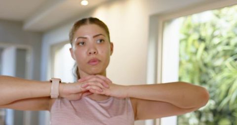 Woman stretching arms before home workout wearing fitness watch and sleeveless top