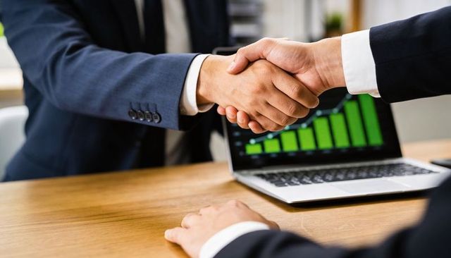 Business partners shaking hands over laptop displaying rising green growth chart