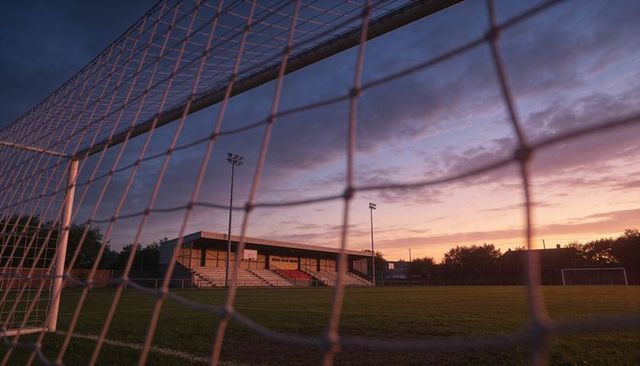 Framing sunset through soccer goal net over empty community stadium stands