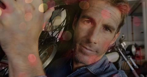 Male Mechanic Holding Motorcycle Wheel with Bokeh Lights Overlay