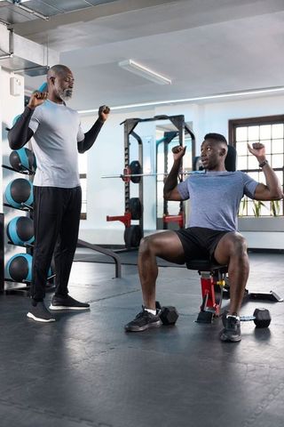 Senior african american trainer spotting adult client bench press strength coaching at modern gym