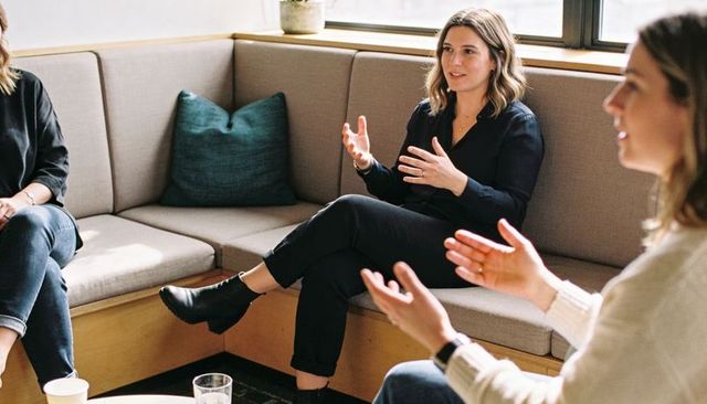 Woman leading team discussion in modern office lounge, gesturing and collaborating over coffee