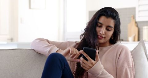 Relaxed mid adult woman engaging with smartphone in modern living room