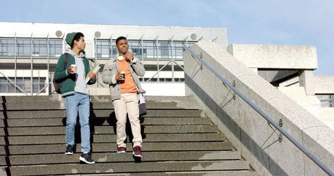 Young friends walking down urban stairs carrying coffee backpacks casual campus lifestyle