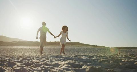 Couple holding hands running on sandy beach at sunset