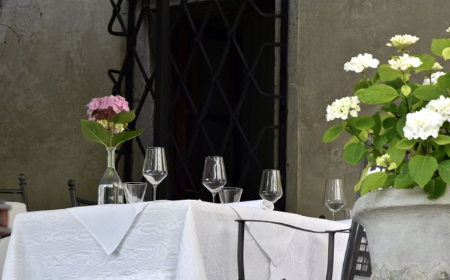 Outdoor dining table elegantly set with white tablecloth, wine glasses, and fresh floral centerpieces is perfect for Europe's patio dining scenes, restaurant ads, catering brochures, social media visuals showcasing fine dining, romantic atmosphere for stylistic setup ideas.