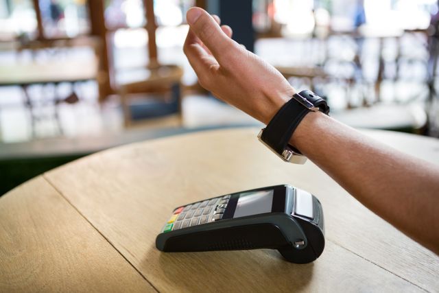 Man's hand using a smart watch for contactless payment at a coffee shop. Represents modern and convenient transaction methods. Ideal for articles or advertisements on fintech, smart technology, and digital wallets.