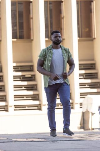 African american man walking in urban plaza holding green striped shirt over gray t-shirt