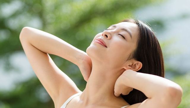 Serene asian woman relaxing outdoors sunlit portrait hands behind neck garden bokeh