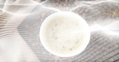 Top-down white mug with frothy coffee on beige woven textile with soft light streaks