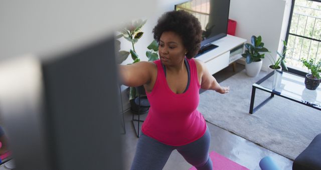 Image of a curvy woman practicing yoga in her living room, demonstrating an active and healthy lifestyle. Ideal for use in articles, blogs, and advertisements promoting fitness, wellness, self-care, home workouts, and inclusivity.