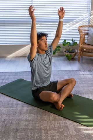 Asian man practicing seated yoga at home in bright minimalist living room