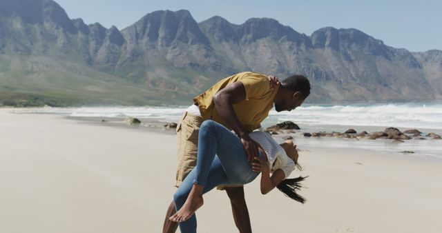 Romantic moment of couple sharing a playful dance on sandy beach with mountains in background. Ideal for travel, relationship, love, summer vacation concepts, and adventure stories.