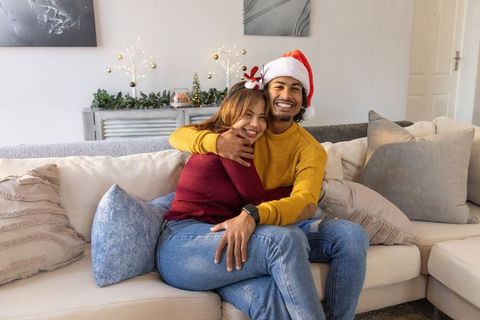 Couple hugging on sofa wearing santa hat and reindeer antlers sharing cozy holiday moment