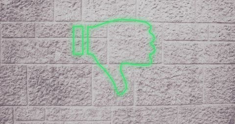 Green neon thumbs down icon on concrete wall