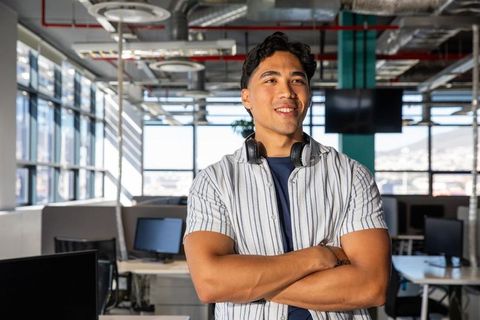 Young asian professional standing with headphones wearing striped shirt in modern office