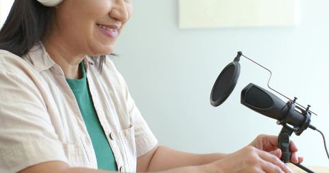 Mature asian woman recording podcast wearing headphones adjusting professional microphone