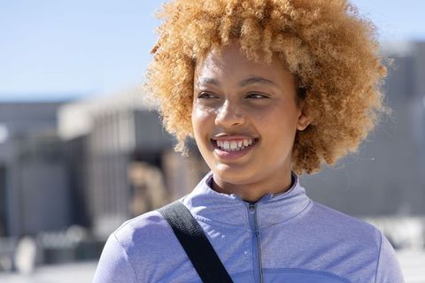 African american woman smiling on campus in purple athletic jacket with crossbody bag